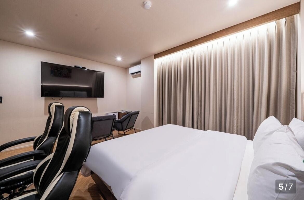 A hotel room with a bed, a TV mounted on the wall, a desk with a chair, and a window with curtains.