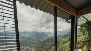 Una habitación con una mesa de madera y una silla, ventanas amplias con vistas a colinas y montañas verdes.