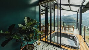 Un cuarto con paredes de vidrio que incluye un jacuzzi, plantas en macetas y vistas a montañas.