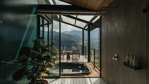 Un interior moderno con techo de madera, planta en maceta, suelo de baldosas y vistas a montañas a través de amplios ventanales.