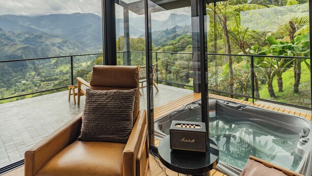 Una habitación moderna con un amplio ventanal, un sillón de cuero, una mesita con un radio y una mesa de vidrio con un banco.
