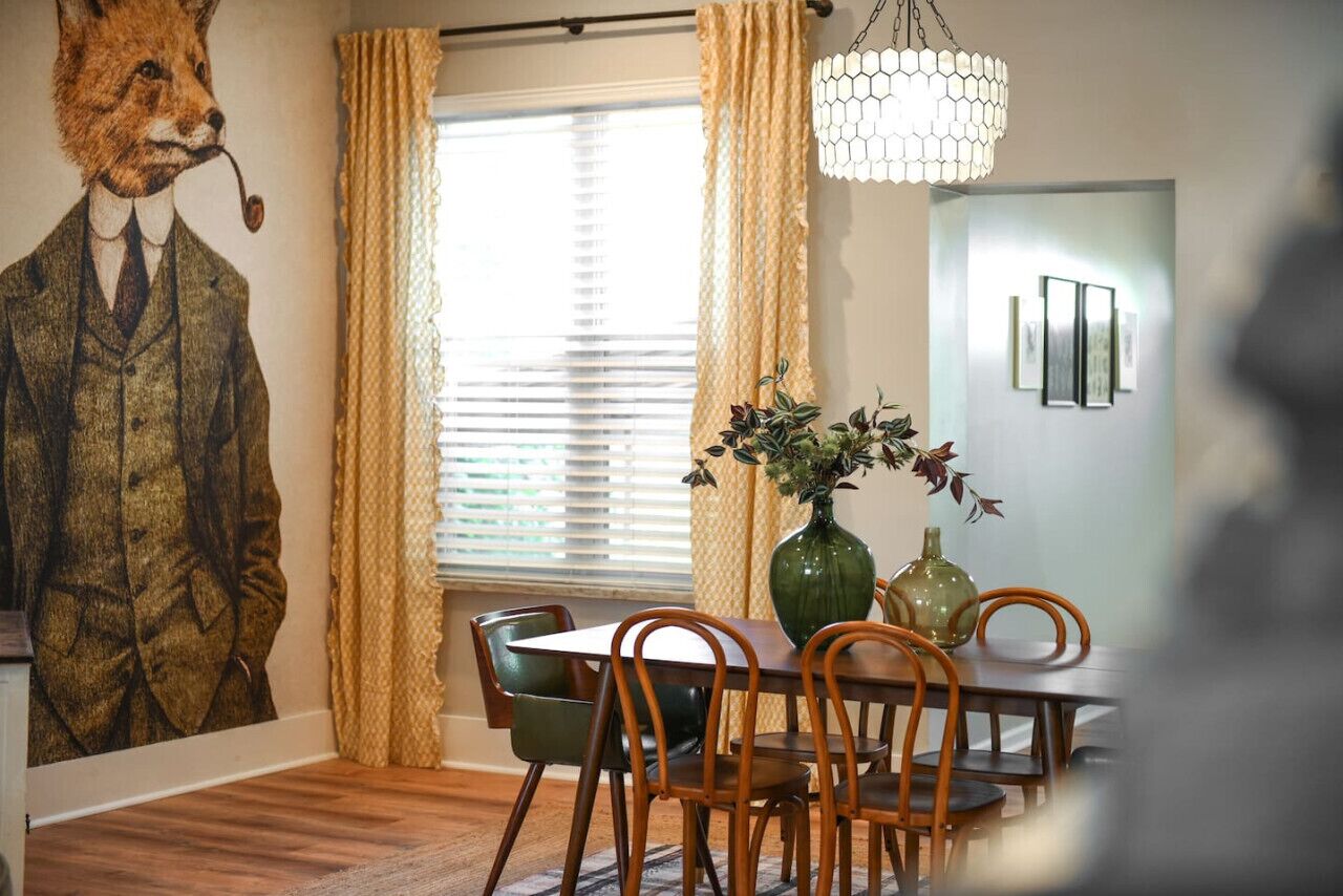 A dining area with a table, chairs, a vase with plants, and a wall mural.