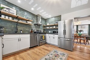 A modern kitchen with white cabinets, stainless steel appliances, and wooden shelves.