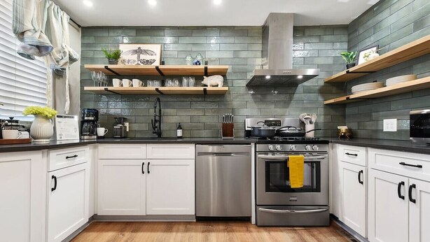 A modern kitchen with white cabinets, a stainless steel dishwasher, an oven, and a stove. There are wooden shelves above the counter holding dishes and glasses. - ★ HostWise Stays ★ Foxy home, off-street parking, new remodel! (Pittsburgh)