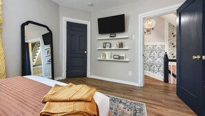 A bedroom with a bed, a TV mounted on the wall, and a door leading to another room. - ★ HostWise Stays ★ Foxy home, off-street parking, new remodel! (Pittsburgh)