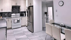 A modern kitchen with white cabinets, stainless steel appliances, and a glass dining table with chairs.