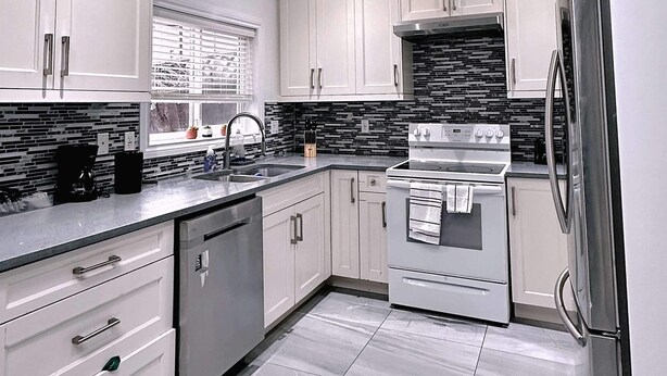 A modern kitchen with white cabinets, a stainless steel refrigerator, and a tiled backsplash.