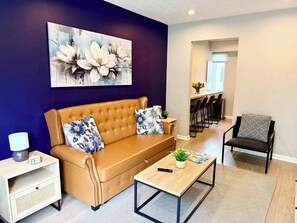 Ein Wohnzimmer mit einer Couch, einem Couchtisch, einem Beistelltisch, einem Sessel und einem Gemälde an der Wand.
