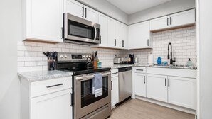 A modern kitchen with white cabinets, stainless steel appliances, and a tiled backsplash. - The Cobbler 's Abode (Columbus)