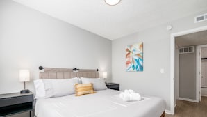 A hotel room with a large bed, two bedside tables, a headboard, a wall-mounted abstract painting, and a door leading to a bathroom. - The Cobbler 's Abode (Columbus)