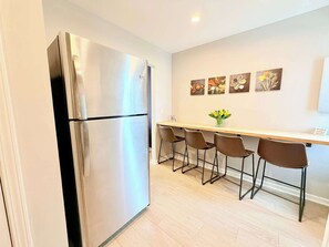 Eine Küche mit einem Edelstahl-Kühlschrank, einer Holztresen mit vier Stühlen und vier Wandbildern.