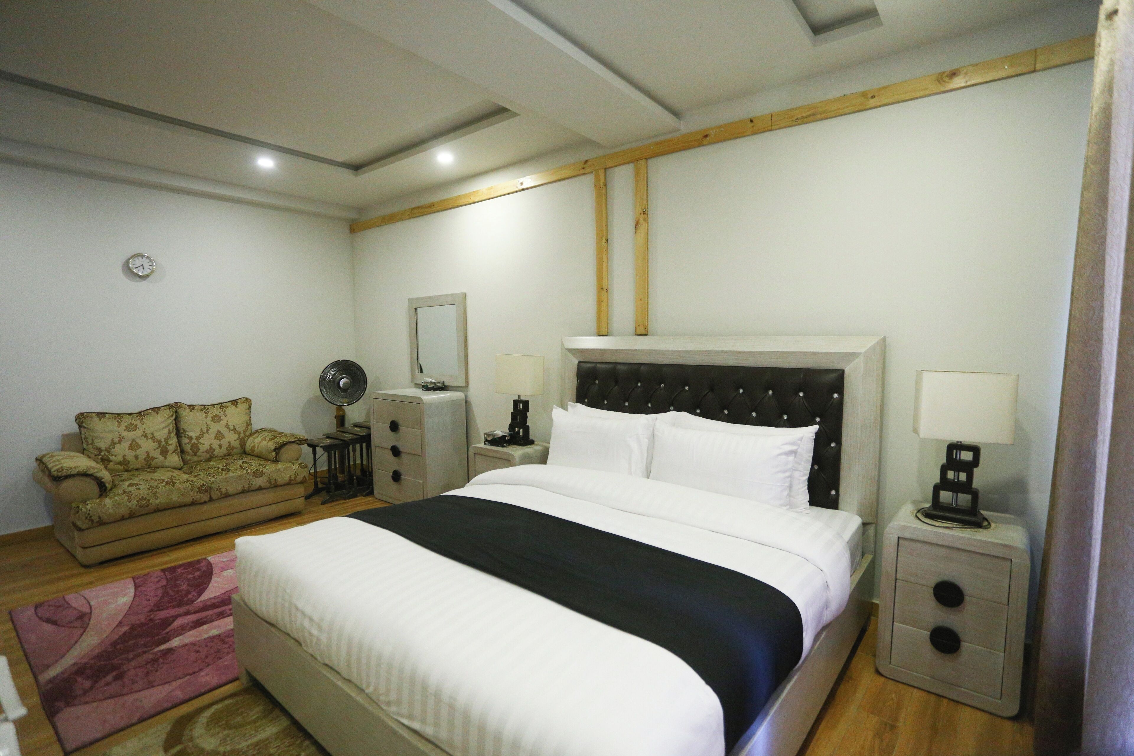 Une chambre à coucher avec un grand lit, un canapé, une table de chevet avec une lampe, un miroir et une horloge au mur.