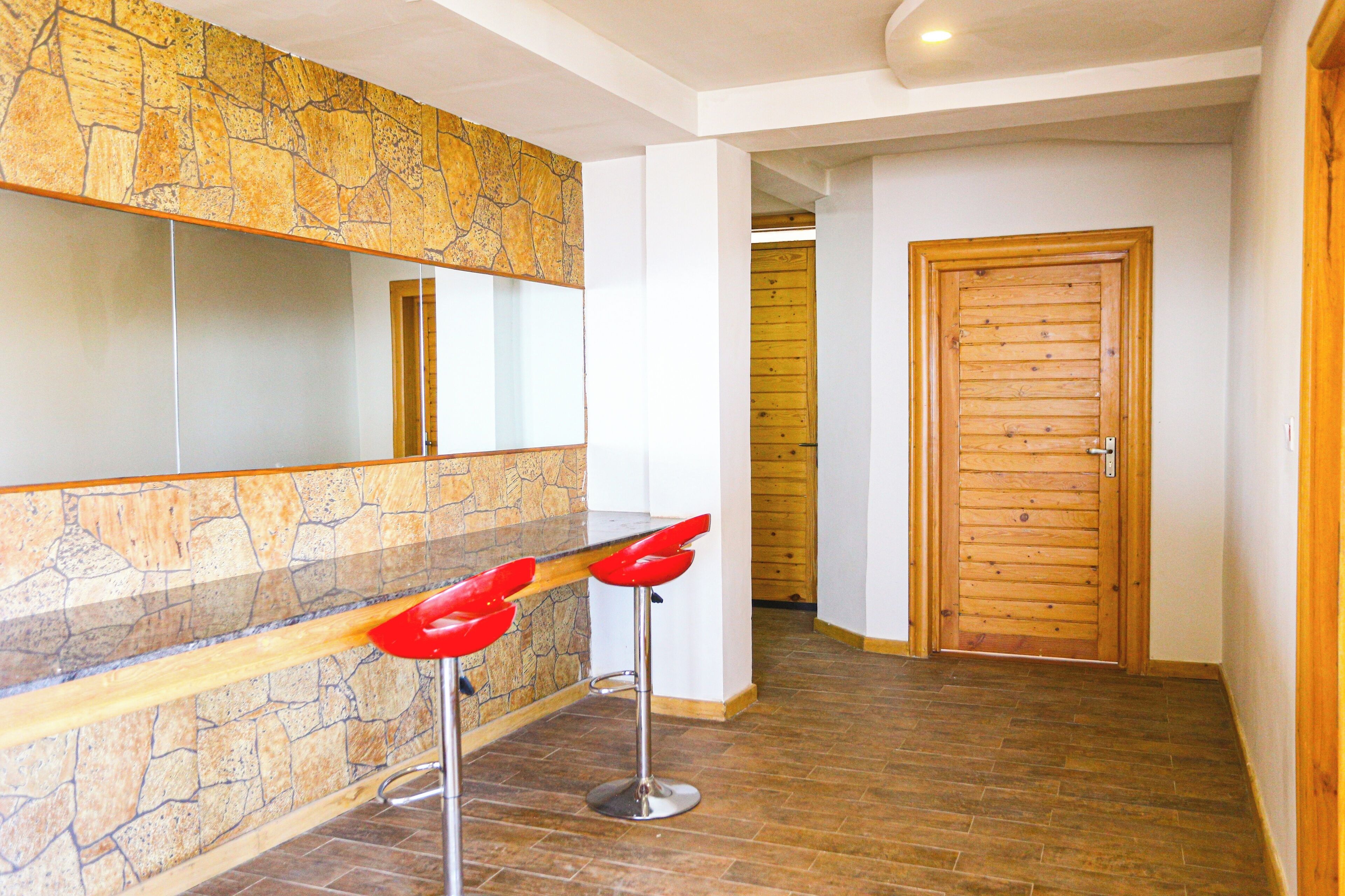 Un interior moderno con una pared de piedra decorativa, una puerta de madera y una zona de bar con taburetes rojos.