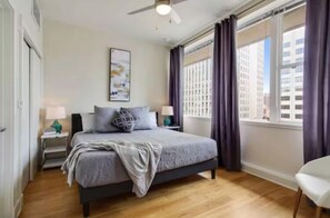 A modern bedroom with a bed, nightstands, a ceiling fan, and a window with curtains. - Legacy Bnb Suites (New Orleans)