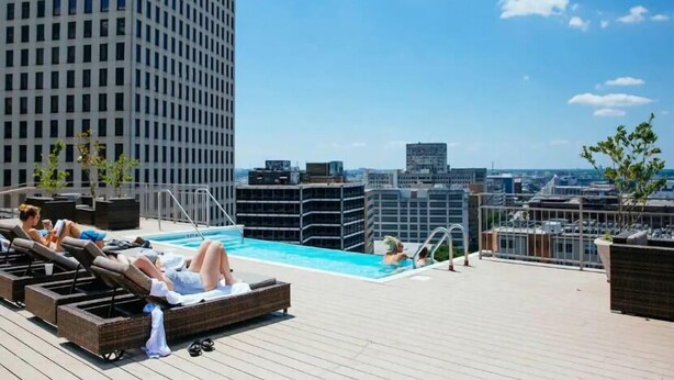Ein Poolbereich auf dem Dach mit Liegestühlen und Blick auf die Skyline der Stadt.