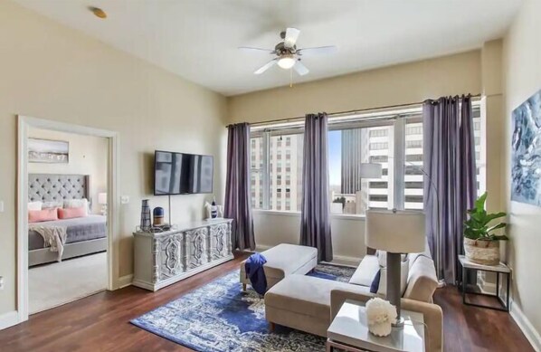 A modern living room with a sofa, a coffee table, a TV, and a ceiling fan. - Legacy Bnb Suites (New Orleans)