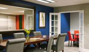 A conference room with a wooden table, grey chairs, a vase with yellow flowers, and a framed picture on the wall. - Legacy Bnb Suites (New Orleans)