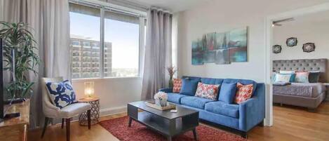 A modern living room with a blue sofa, a coffee table, a chair, and a large window with curtains.