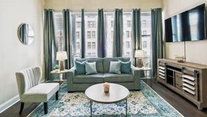 Ein Wohnzimmer mit einer Couch, einem Couchtisch, einem Fernseher und Blick auf Gebäude durch große Fenster.