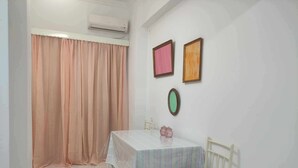 Een kleine kamer met een bed, een tafel met tafelkleed, een stoel en een raam met gordijnen.
