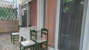 Een terras met een tafel en vier stoelen, een schuifdeur en een groene hekwerk van gaas.