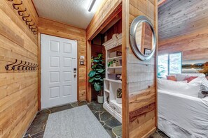 Un intérieur en bois avec une porte blanche, un miroir, un lit avec une literie blanche et une plante en pot.