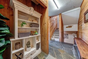 A wooden interior with a staircase, stone flooring, and shelves with decorative items.