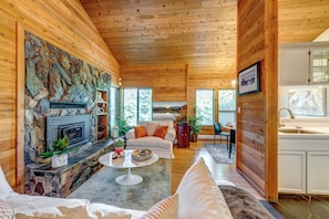 Un intérieur de chalet chaleureux avec une cheminée en pierre, des murs en bois, un coin repas et une cuisine.