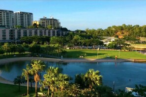A hotel with a large pool surrounded by palm trees and greenery, with modern buildings in the background. - Zen Bridgeport Waterfront Balcony Dining - Pool (Darwin)