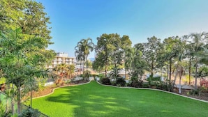 A well-maintained lawn with a curved pathway, surrounded by various trees and shrubs, leading to a building with multiple floors in the background. - Downtown Delight 2BR Getaway Pool (Darwin)