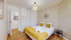 A bedroom with a bed, a bedside table, a wall clock, and a door leading to another room.