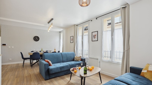 A modern living room with a blue sofa, dining table, and a small coffee table with drinks.