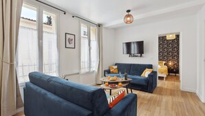 A modern living room with a blue sofa, a coffee table with drinks, and a TV mounted on the wall.