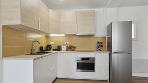 A modern kitchen with white cabinets, a stainless steel refrigerator, a built-in oven, and a sink.