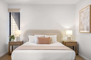 Une chambre d’hôtel avec un grand lit, deux tables de chevet, une fenêtre donnant sur un beau paysage et un tableau encadré au mur.