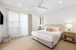 A bedroom with a bed, a ceiling fan, a bedside table with a lamp, and a window with curtains.