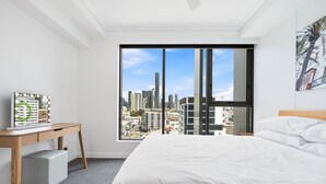 A modern hotel room with a large window, a bed, a desk, and a city view. - Chic 1 Bed Inner-City Retreat with Pool and Views (Fortitude Valley)