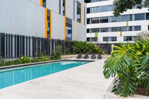 Un edificio moderno con piscina, mobiliario exterior y abundante vegetación.