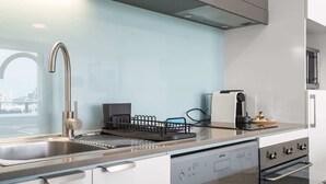 A modern kitchen with a stainless steel sink, a dishwasher, an oven, and a coffee machine. - Chic 1 Bed Inner-City Retreat with Pool and Views (Fortitude Valley)