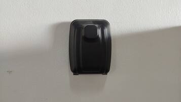 A white wall with a black object mounted on it, possibly a light switch or a control panel.