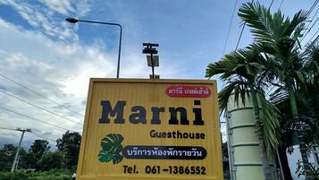 A yellow signboard for Marni Guesthouse with Thai text and a contact number.