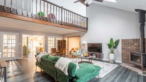 Un salon spacieux avec un canapé vert, une cheminée et un balcon doté d’une balustrade en bois.