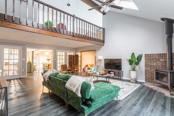 A spacious living room with a green sofa, a fireplace, and a balcony with a wooden railing.