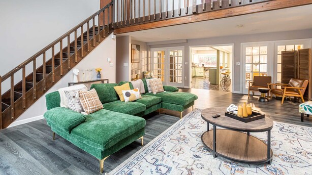 Un vaste espace de vie comprenant un canapé d’angle vert, un escalier en bois et un coin repas avec des meubles modernes.