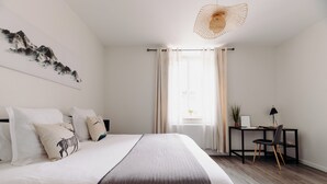 A bedroom with a large bed, a desk with a chair, and a window with curtains.