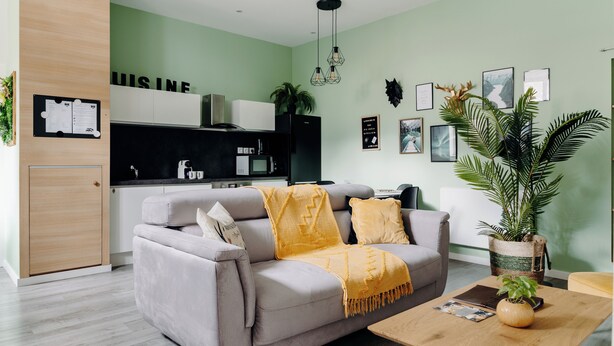 A modern living room with a grey sofa, a wooden coffee table, and a kitchen area in the background.