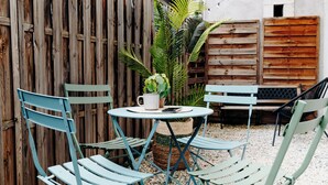 A small outdoor seating area with a round table and four chairs, surrounded by a wooden fence and a white wall.