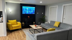 A living room with a grey sofa, a yellow armchair, a coffee table, and a flat-screen TV mounted on the wall. - The Creek House Spacious 4-bedroom house in brilliant Vancouver with WiFi (Vancouver)