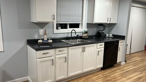A modern kitchen with white cabinets, a black countertop, a sink, a coffee maker, and a dishwasher. - The Creek House Spacious 4-bedroom house in brilliant Vancouver with WiFi (Vancouver)