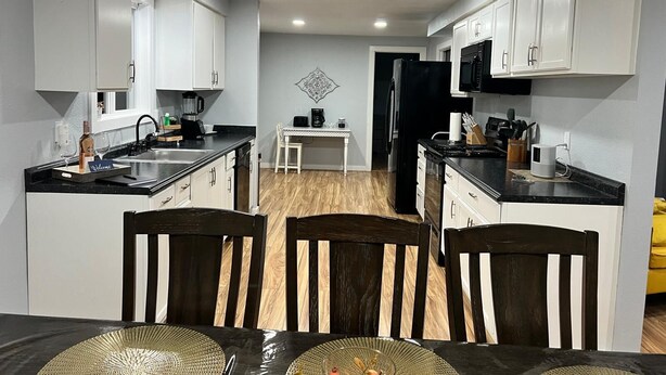 A modern kitchen with white cabinets, a black refrigerator, and a dining area with two wooden chairs and a table. - The Creek House Spacious 4-bedroom house in brilliant Vancouver with WiFi (Vancouver)